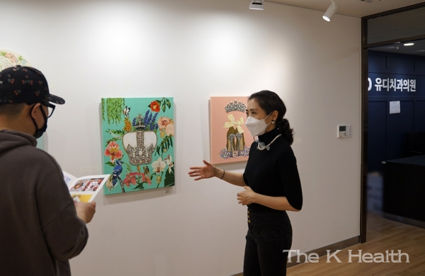 문민정 작가(오른쪽)가 유디갤러리를 찾은 환자에게 작품을 소개하는 모습(사진제공 : 유디치과)